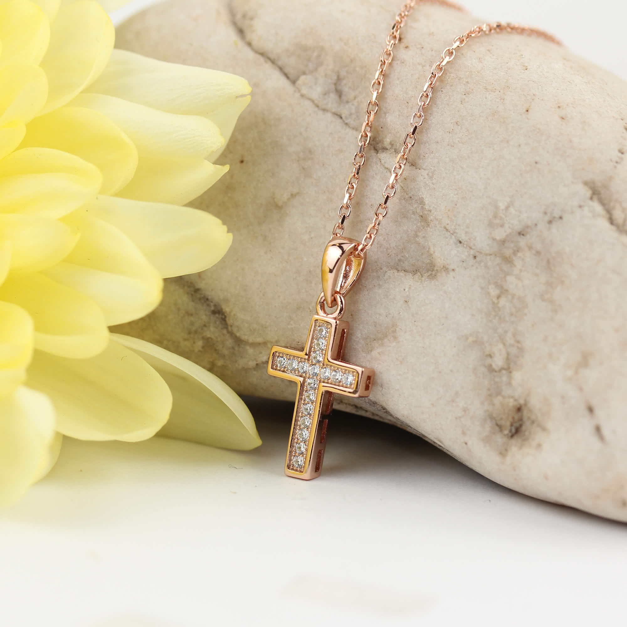 Rose Gold Plated Cross presented next to flower and ornamental stone